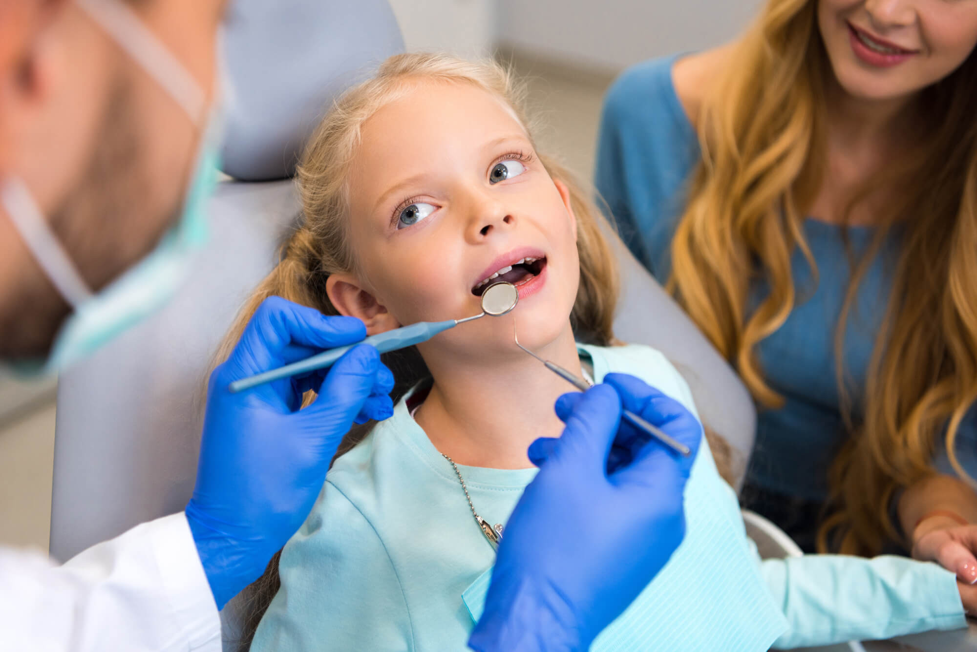a Pediatric Dentist Monsey New York checks a little girl's teeth while her mother looks on